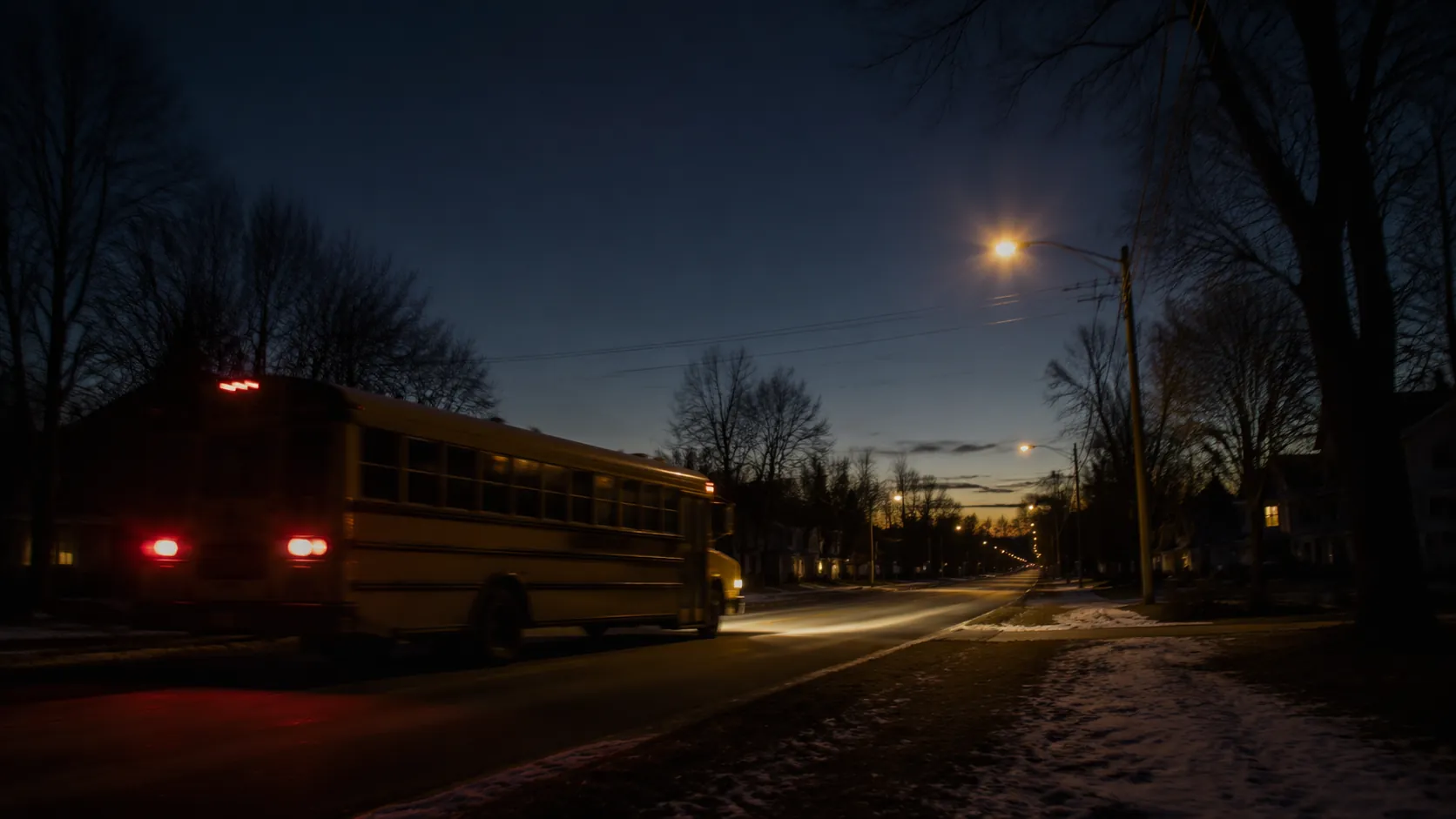 A yellow school bus traveling on a dark winter morning street under lit streetlights