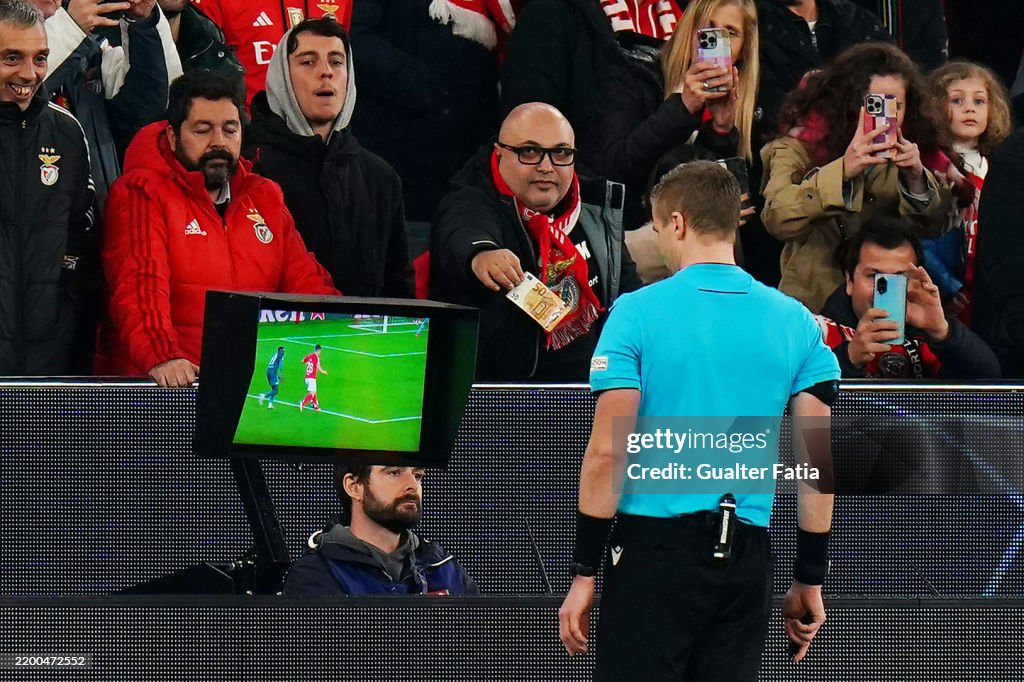 Benfica supporter offering a fifty-euro note toward referee Glenn Nyberg at the pitchside VAR monitor