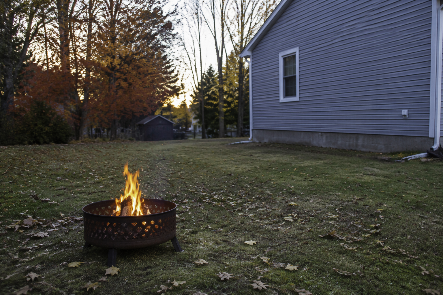 Residential backyard with a metal fire pit positioned away from a house