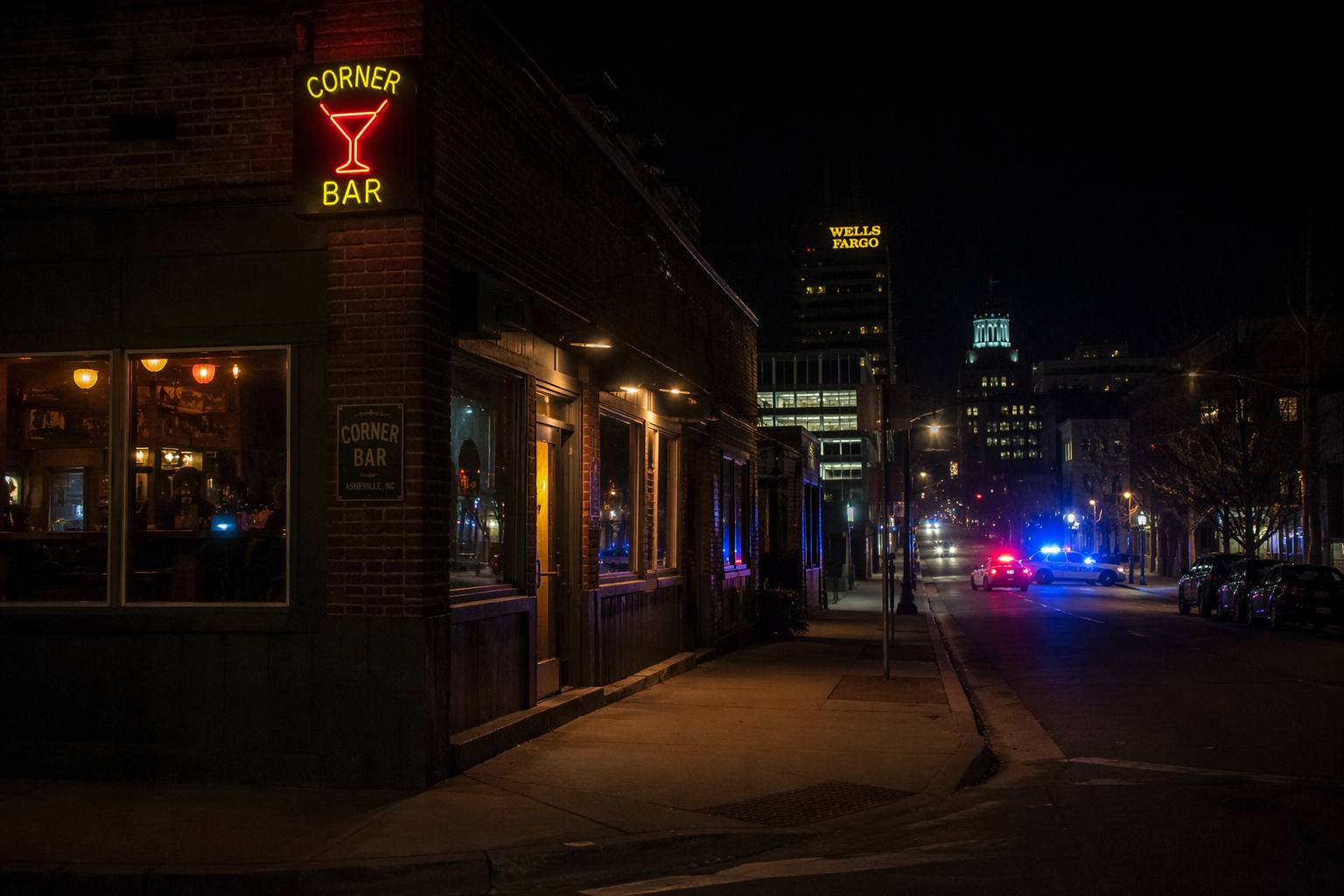 Nighttime downtown Asheville bar exterior with police lights in the distance