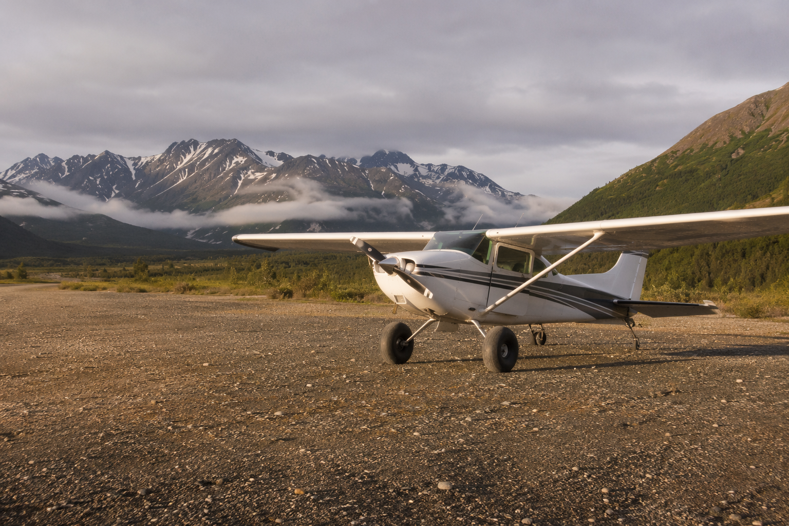 Small Cessna bush plane parked on a remote gravel airstrip in rural Alaska