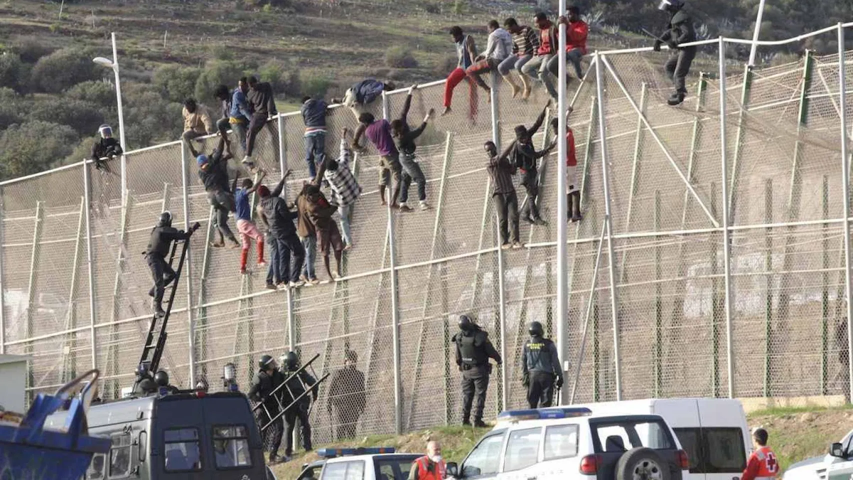 People attempting to climb the tall metal border fence at the Ceuta or Melilla frontier during a mass crossing