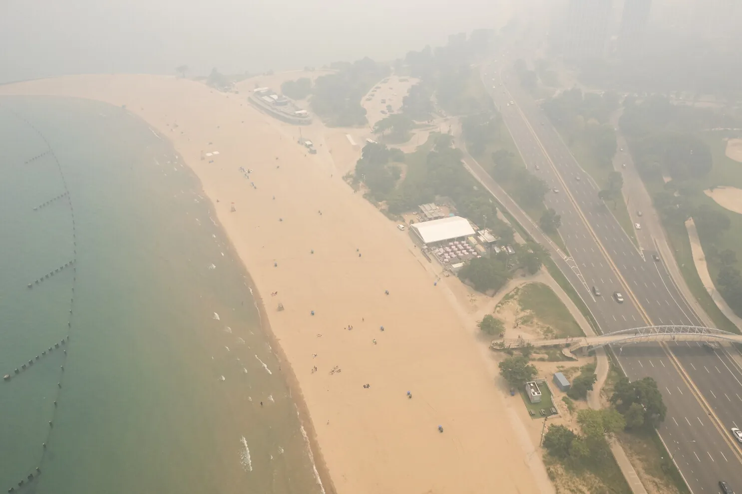 Chicago street and skyline shrouded in orange-gray wildfire-smoke haze with an air quality alert sign visible