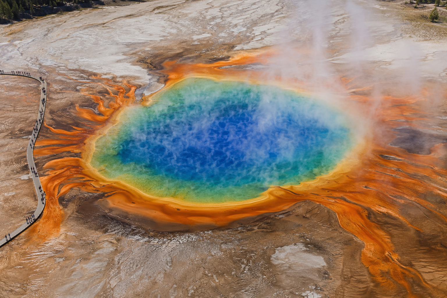 Aerial view of Grand Prismatic Spring with a boardwalk along one edge and colorful thermal rings in the water